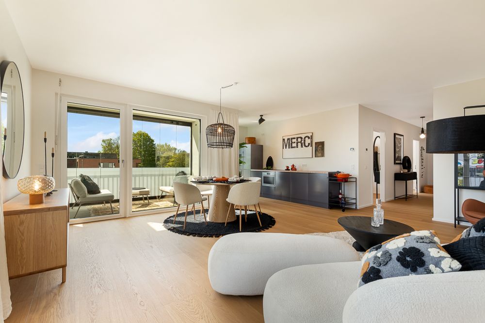 Helles Wohnzimmer mit Essbereich, offener Küche und Zugang zu einem Balkon.