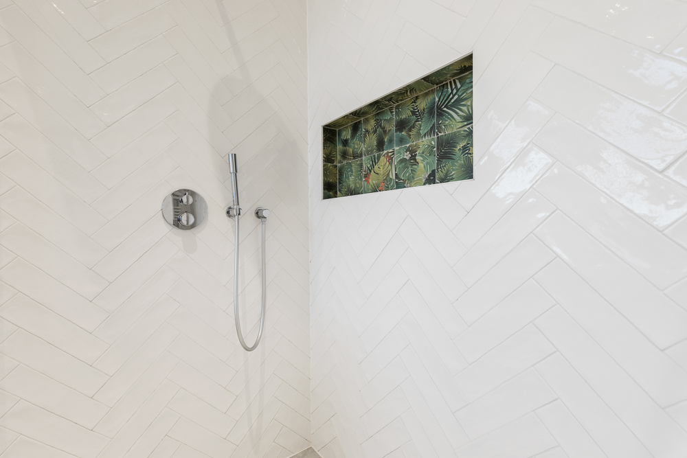 Weiße geflieste Dusche mit Nische und tropischen Fliesen darin.