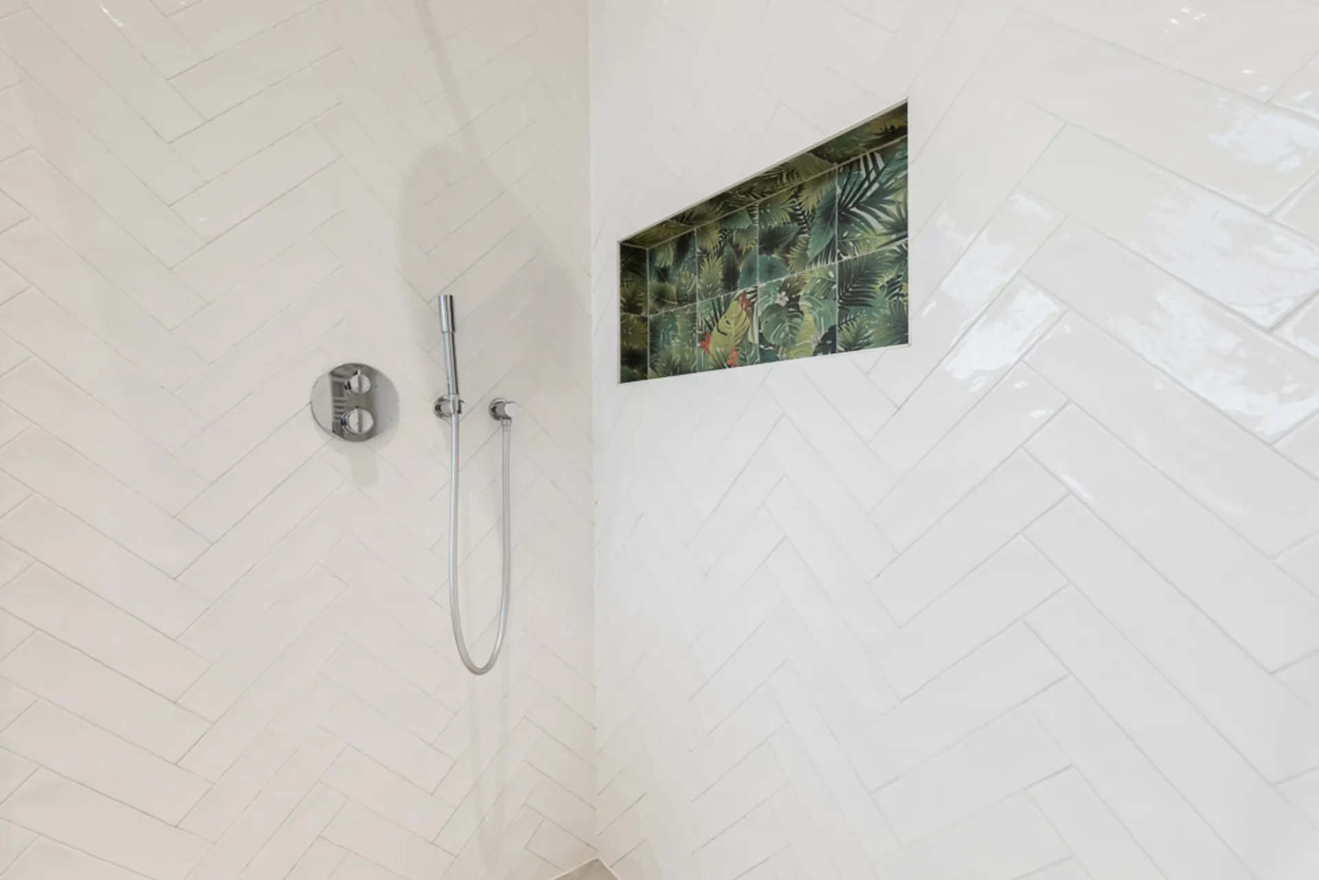 Weiße geflieste Dusche mit Nische und tropischen Fliesen darin.