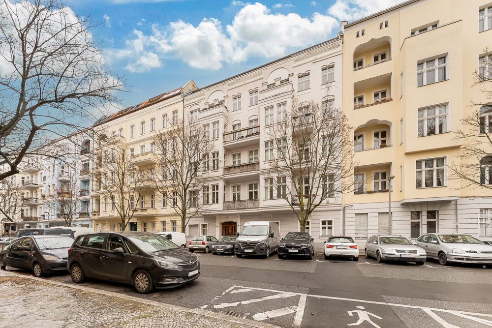 Mehrstöckige Wohnhäuser mit Balkonen, Bäumen und parkenden Autos an der Straße.