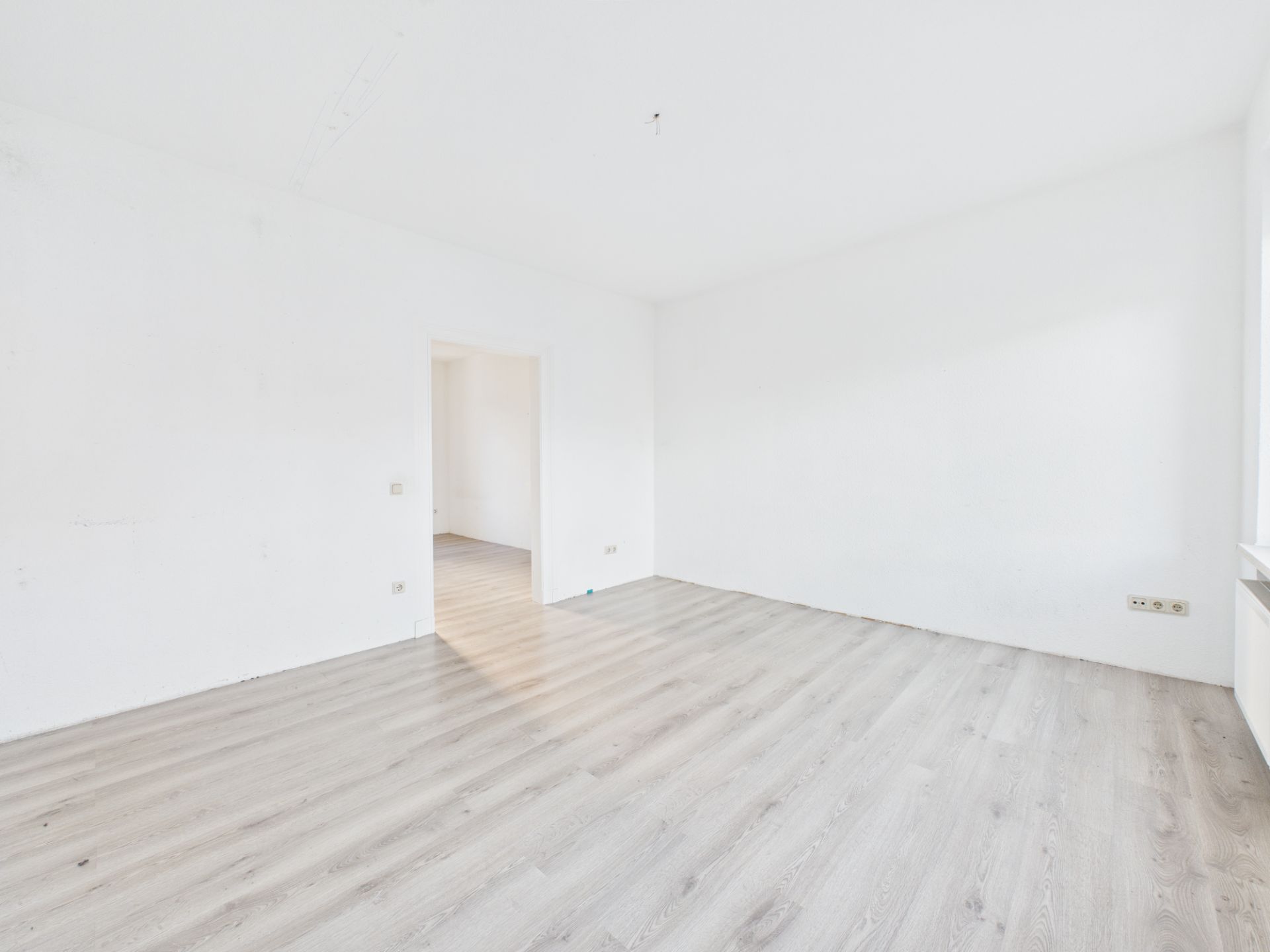 Heller, leerer Raum mit weiß gestrichenen Wänden und hellem Holzboden.
