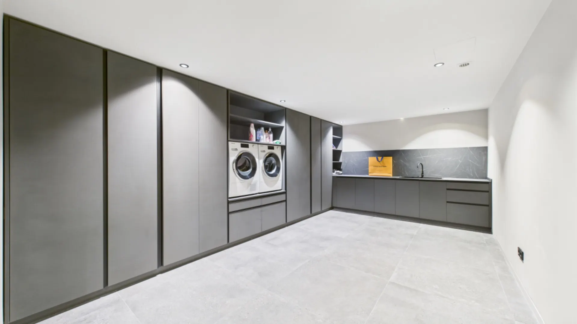 Moderner Hauswirtschaftsraum mit Waschmaschine, Trockner und grauen Einbauschränken.