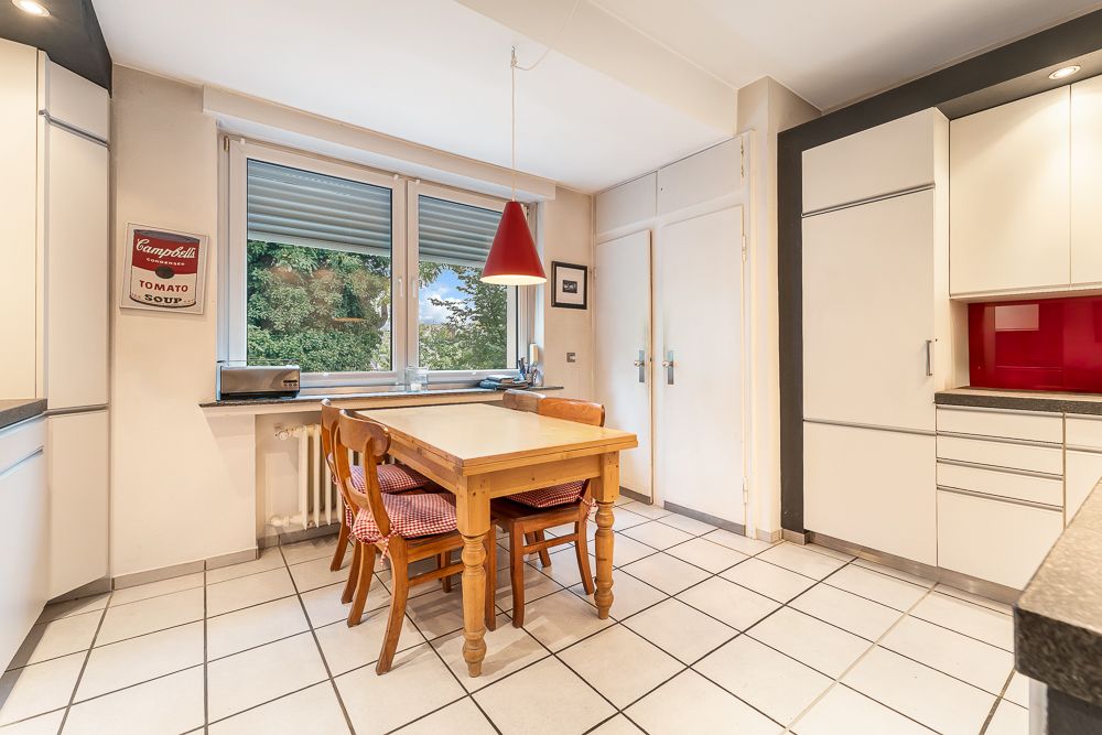 Helle Küche mit Holztisch, vier Stühlen, weißen Schränken und großem Fenster.