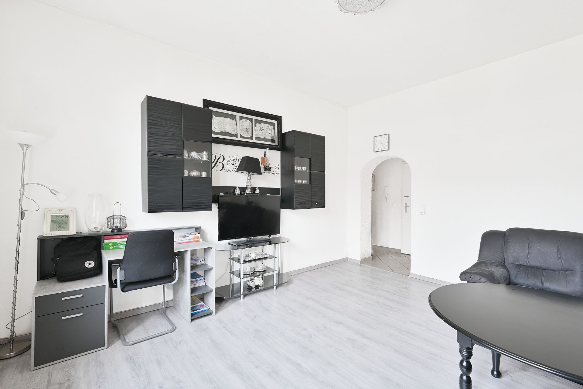 Modernes Wohnzimmer mit Schreibtisch, schwarzem Sofa, Wandregalen und Fernseher.