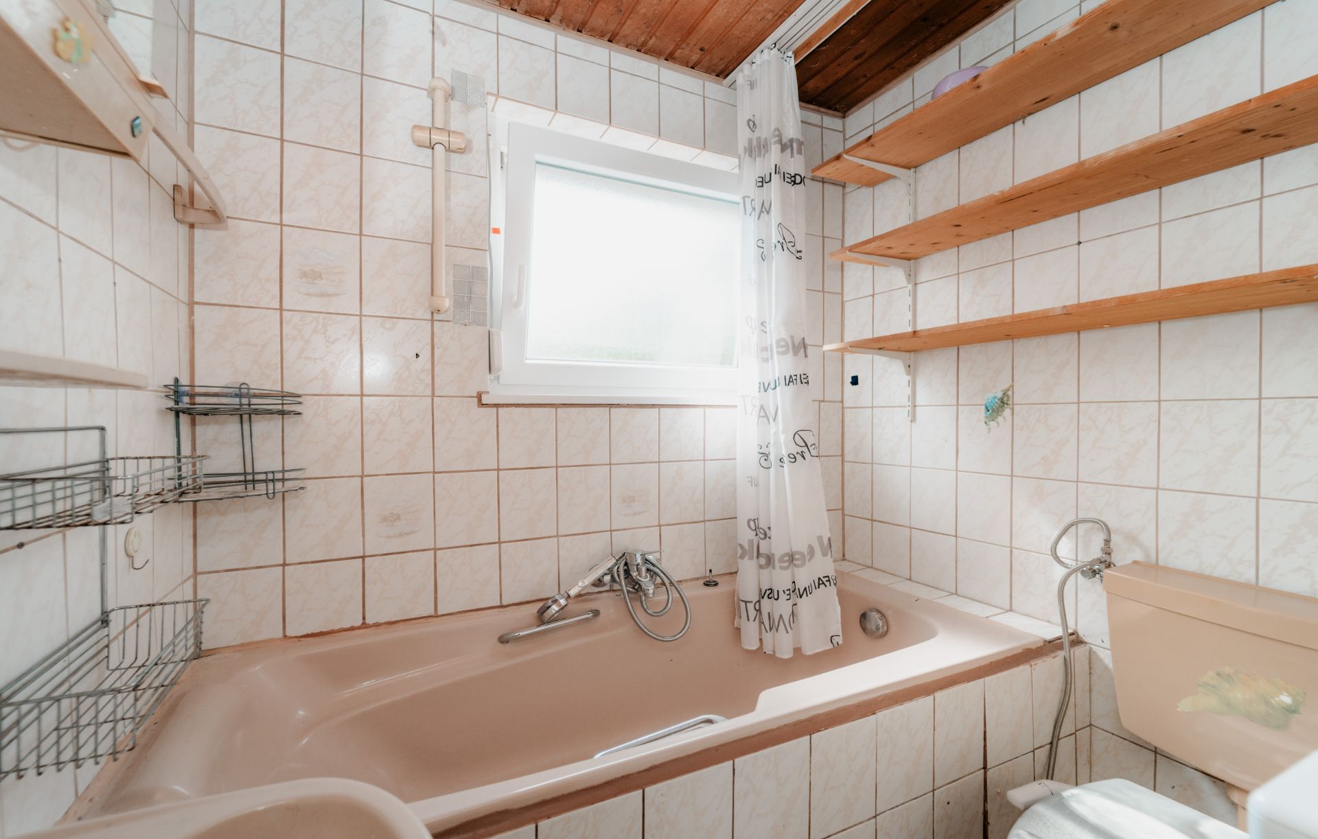 Kleines Badezimmer mit Badewanne, Fliesenwänden, Regal, Fenster und Duschvorhang.