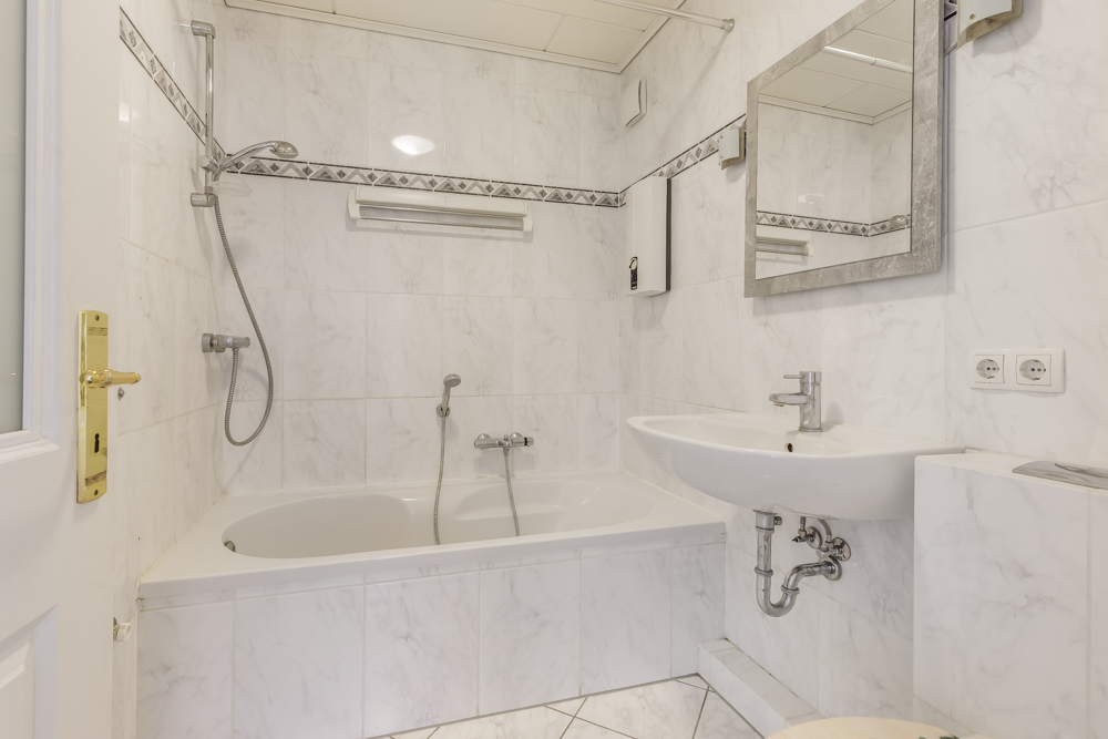 Helles Badezimmer mit Badewanne, Dusche, Waschbecken, Spiegel und weißen Fliesen.