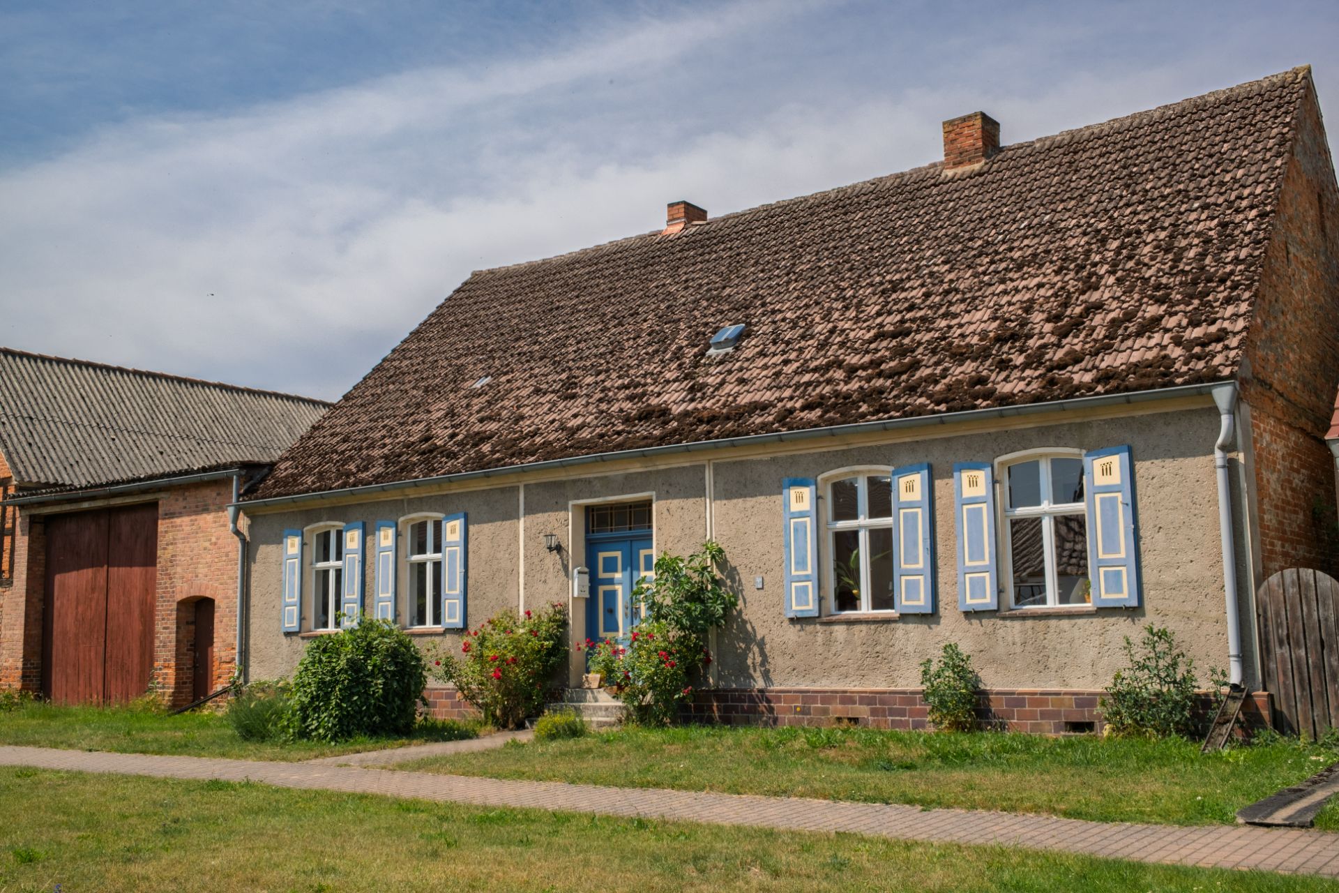 Altes Einfamilienhaus mit blau-weißen Fensterläden und Garten vor dem Haus.