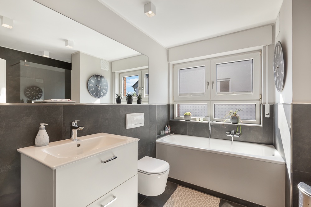 Modernes Badezimmer mit Badewanne, Waschbecken, WC und großem Fenster.