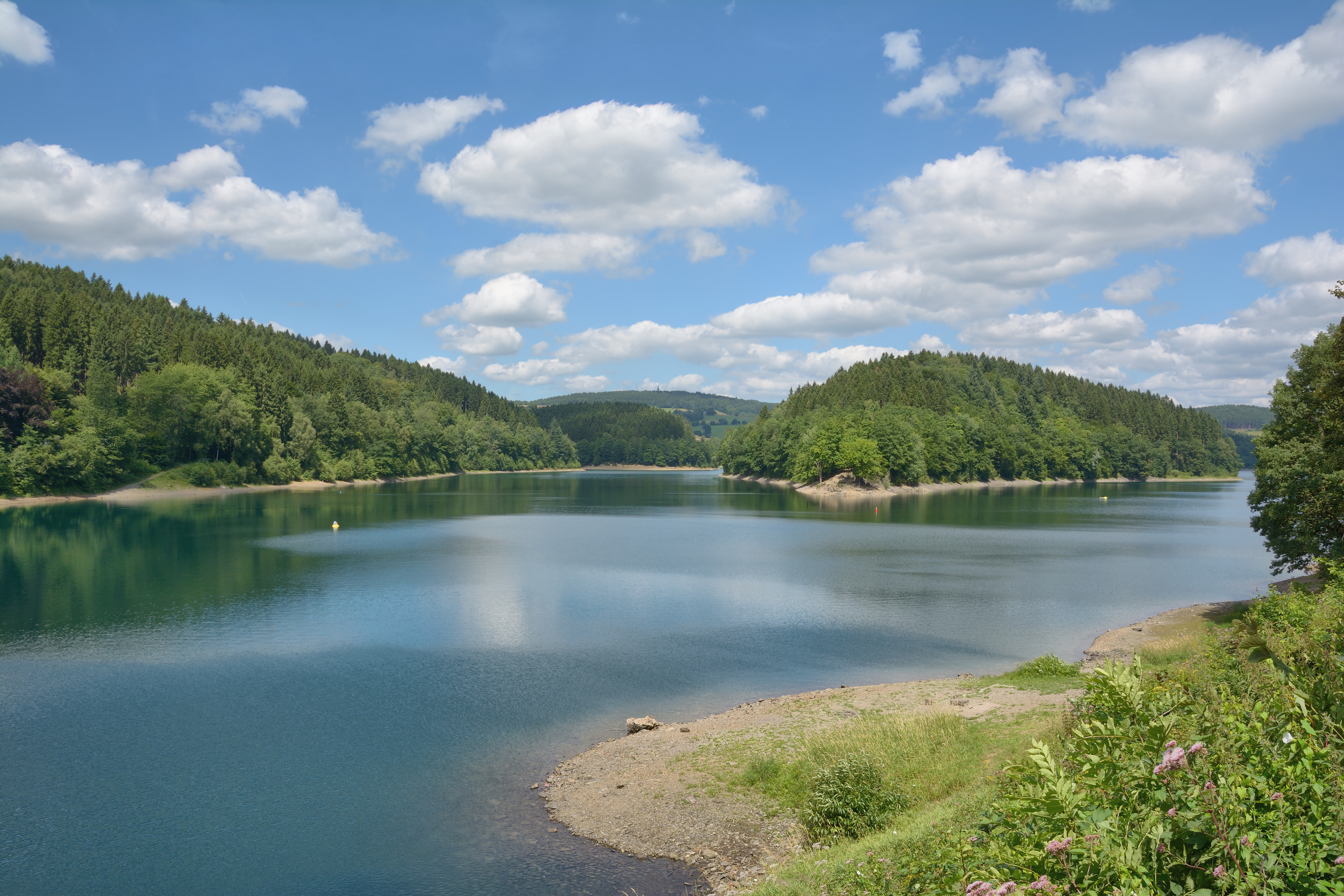 See mit bewaldeten Ufern, klarem Himmel und einigen Wolken.