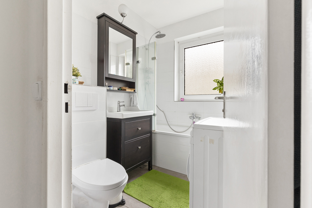 Helles Badezimmer mit Toilette, Waschbecken, Badewanne, Waschmaschine und grünem Teppich.