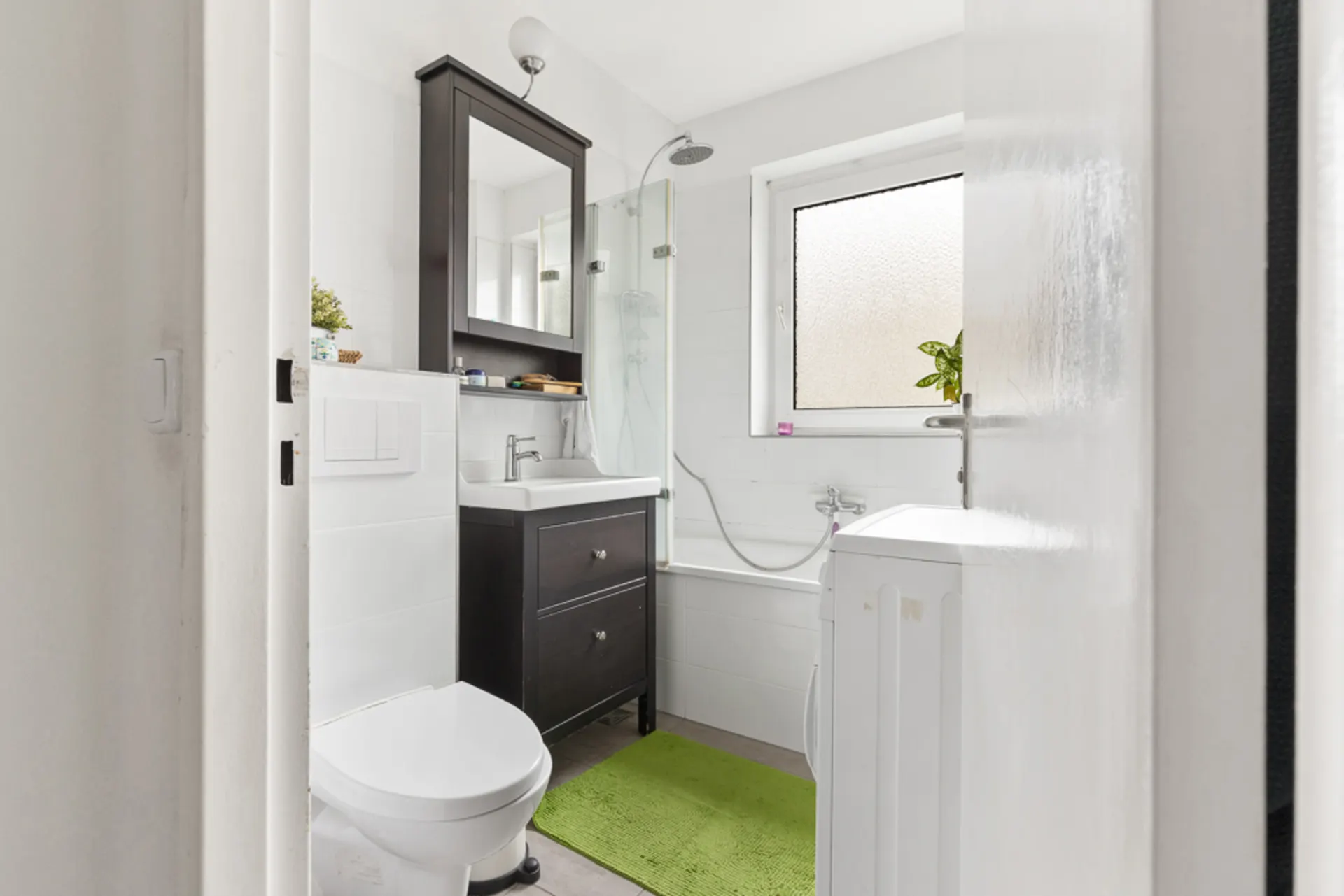 Helles Badezimmer mit Toilette, Waschbecken, Badewanne, Waschmaschine und grünem Teppich.