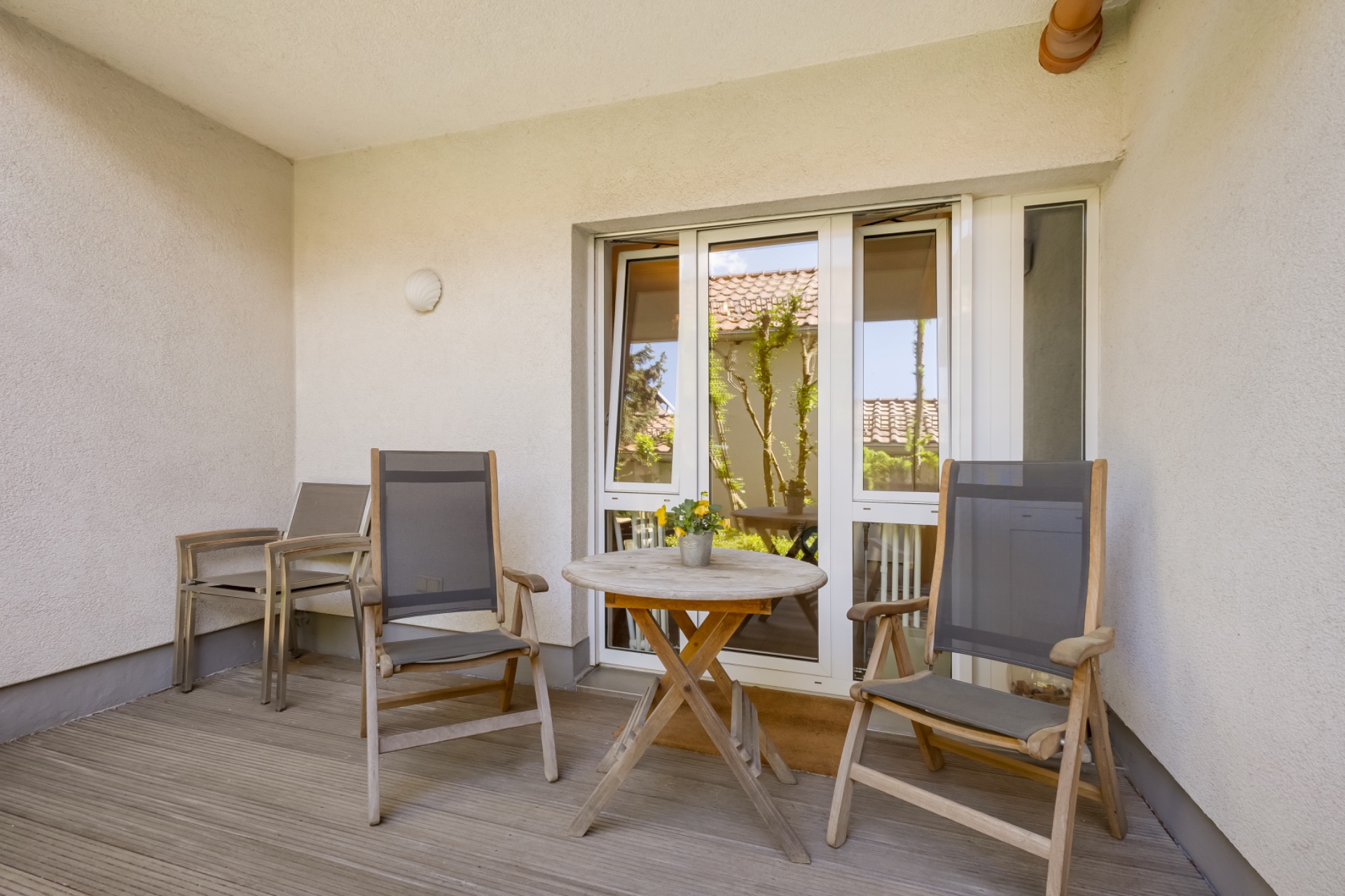 Überdachter Balkon mit zwei Stühlen, kleinem runden Tisch und Pflanze in Blumentopf.