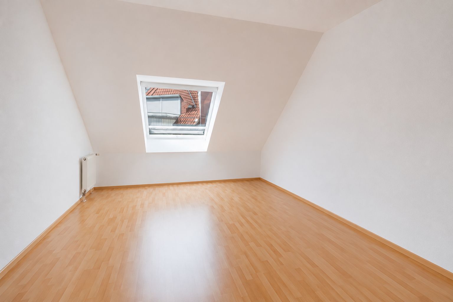 Leerer Raum mit schrägen Wänden, Dachfenster und hellem Holzfußboden.