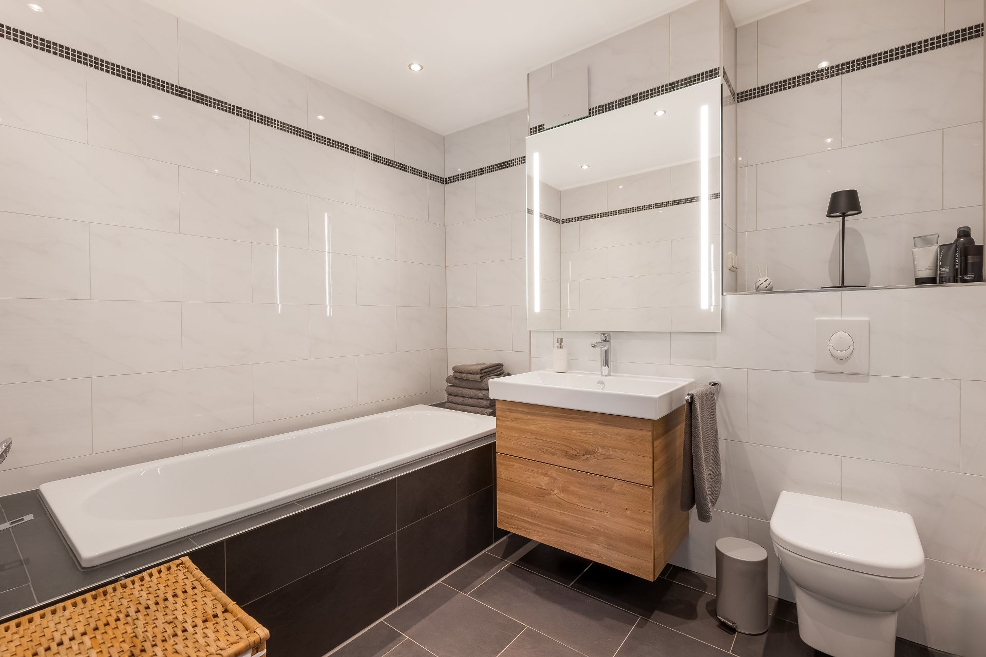 Modernes Badezimmer mit Badewanne, Waschbecken, Spiegel, Toilette und gefliestem Boden.
