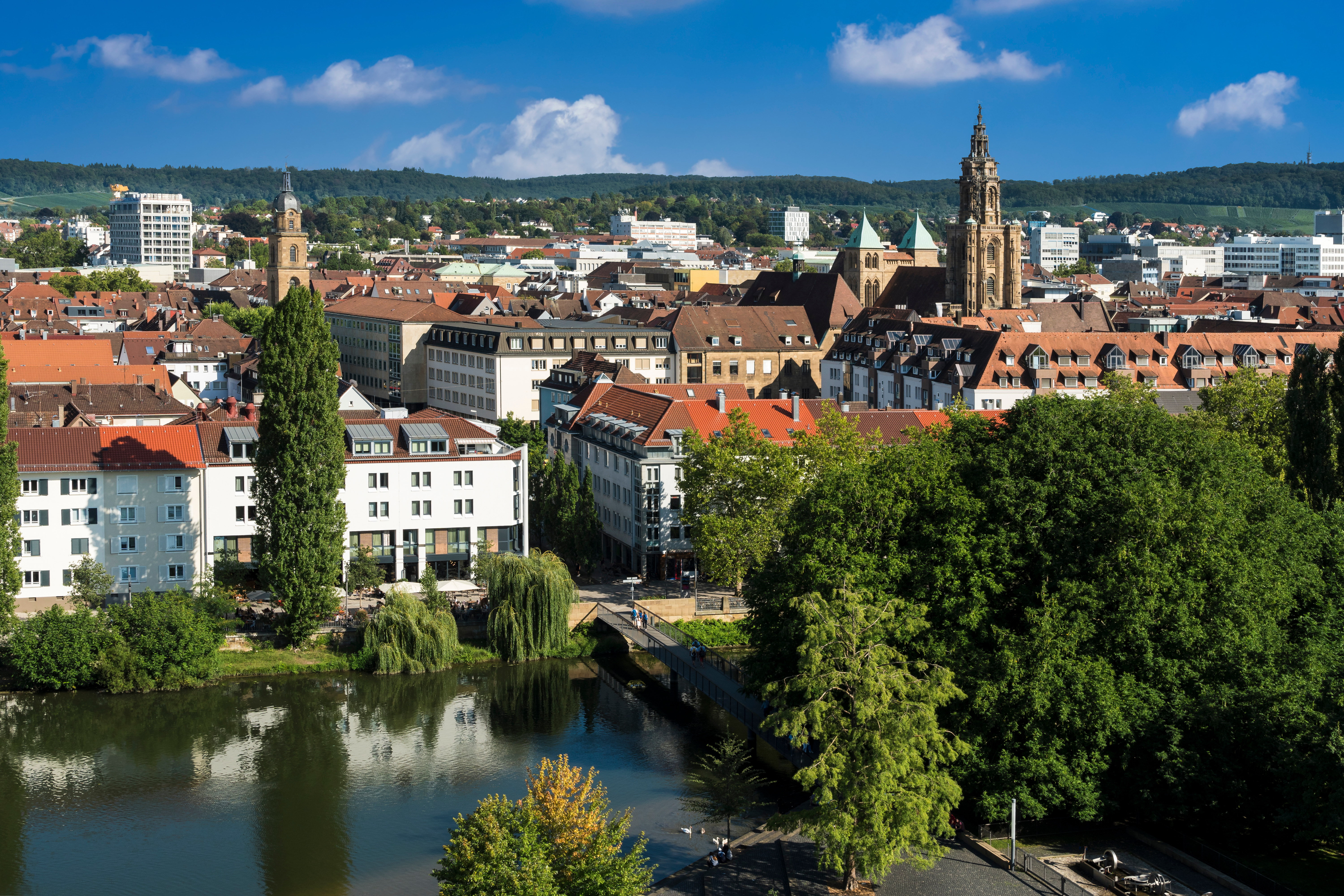 Stadtansicht mit Fluss, Bäumen und Wohngebäuden im Vordergrund.