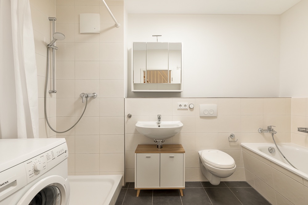 Modernes Badezimmer mit Dusche, Waschmaschine, Waschbecken, Spiegel, WC und Badewanne.