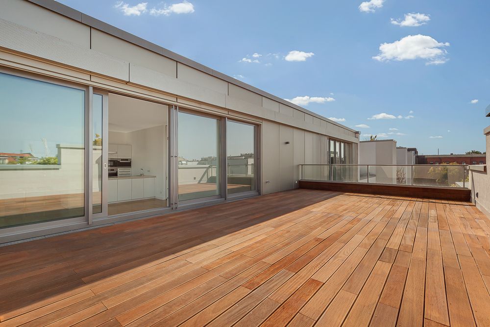 Große Dachterrasse mit Holzboden und Glasgeländer, angrenzend an eine Wohnung mit großen Schiebetüren.