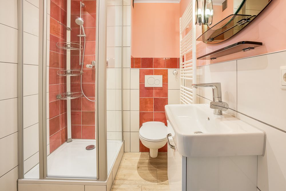 Modernes Bad mit Dusche, Wandtoilette und Waschbecken, rote Fliesen und großer Spiegel.