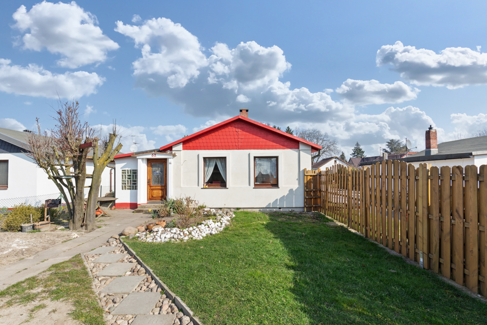 Kleines Einfamilienhaus mit rotem Giebel, Holzzaun und gepflegtem Garten.