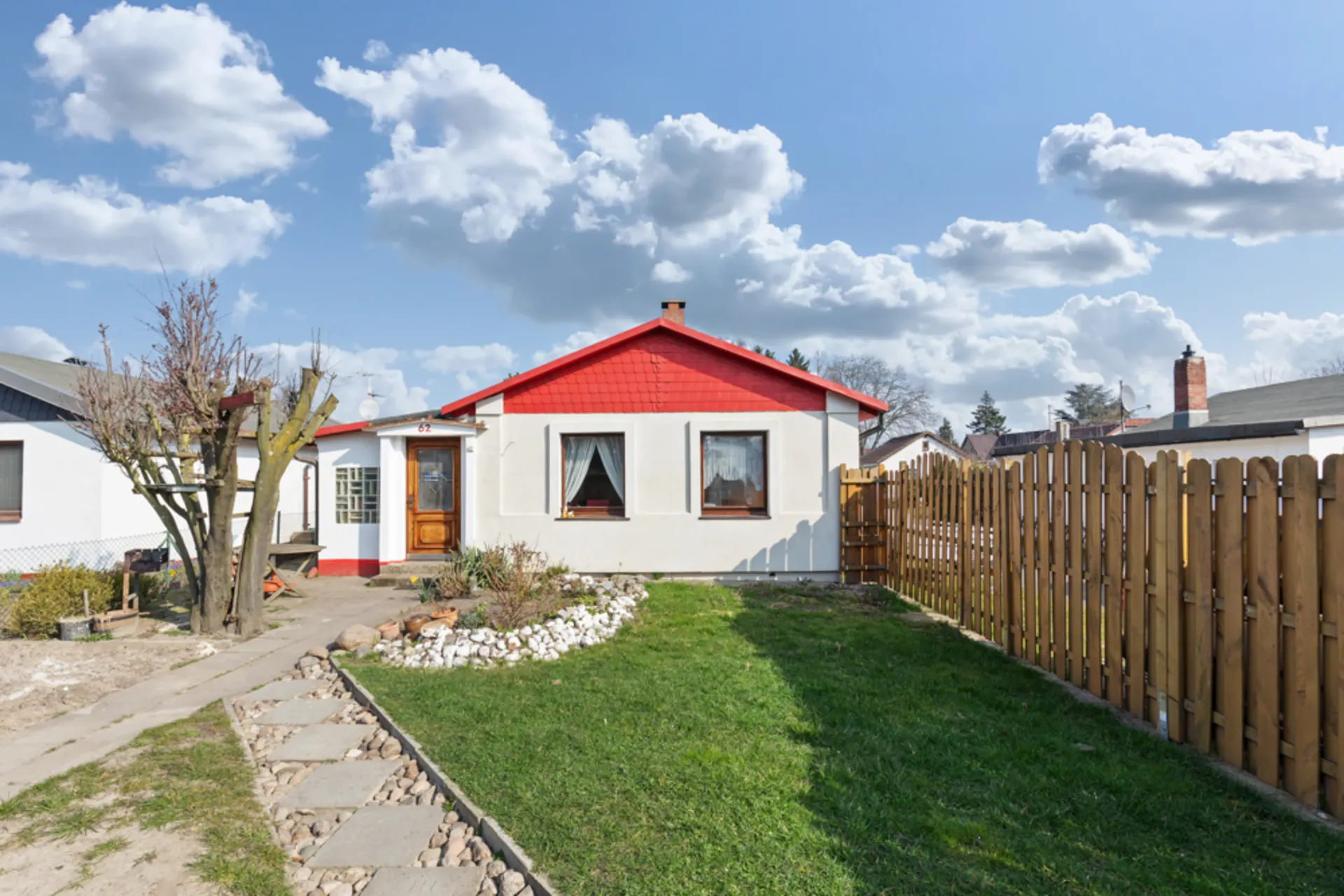 Kleines Einfamilienhaus mit rotem Giebel, Holzzaun und gepflegtem Garten.