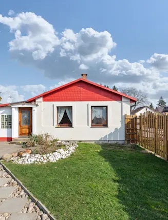 Kleines Einfamilienhaus mit rotem Giebel, Holzzaun und gepflegtem Garten.