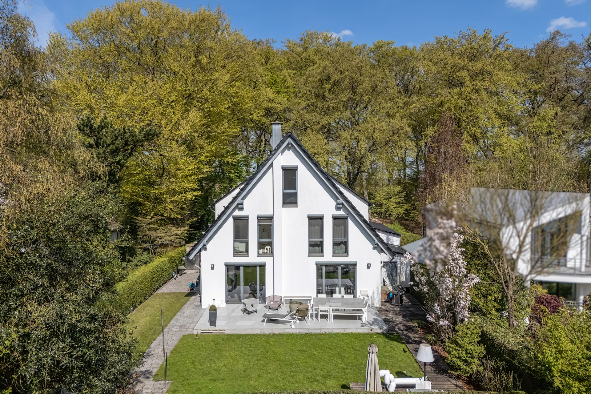 Modernes weißes Wohnhaus mit Terrasse und Garten, umgeben von Bäumen.