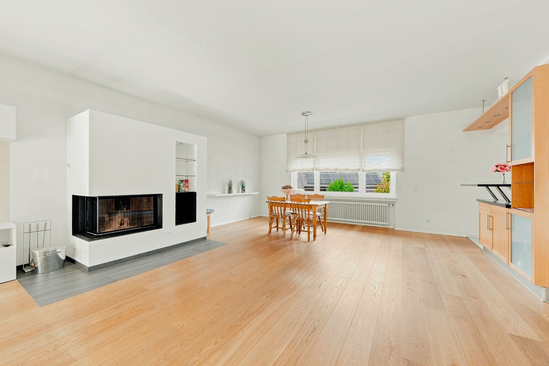 Helles Wohnzimmer mit Kamin, Essbereich, Holzboden und großem Fenster.