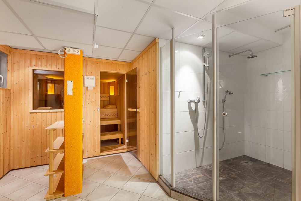 Helles Bad mit begehbarer Dusche und Holzsauna auf gefliestem Boden.