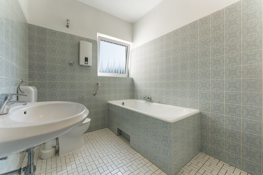Helles Badezimmer mit Badewanne, Waschbecken, Toilette und gemusterten Fliesen.