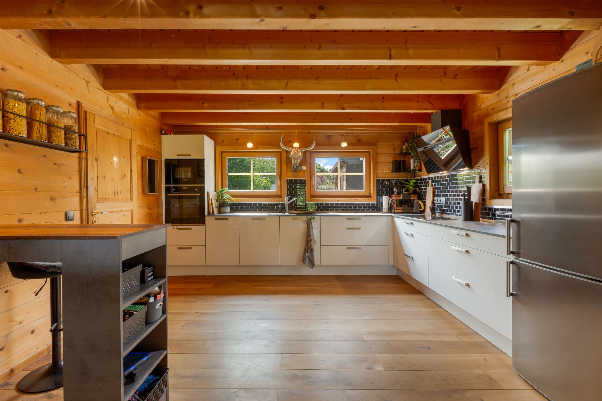 Moderne Holzküche mit weißen Schränken, großem Kühlschrank und zwei Fenstern über der Spüle.
