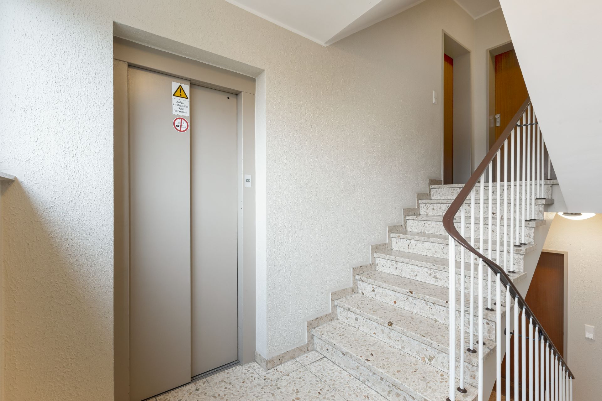 Treppenhaus mit Aufzug und zwei Wohnungstüren in einem Wohngebäude.