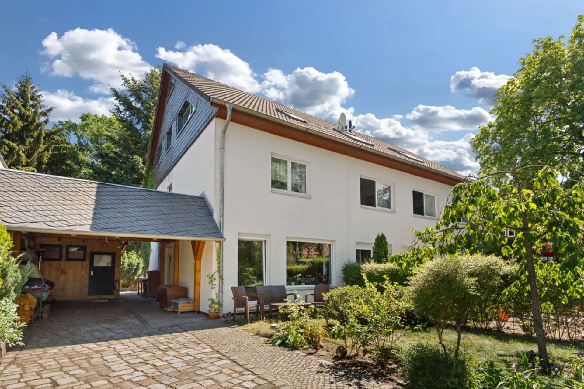 Modernes weißes Wohnhaus mit Garten und überdachtem Carport bei sonnigem Wetter.