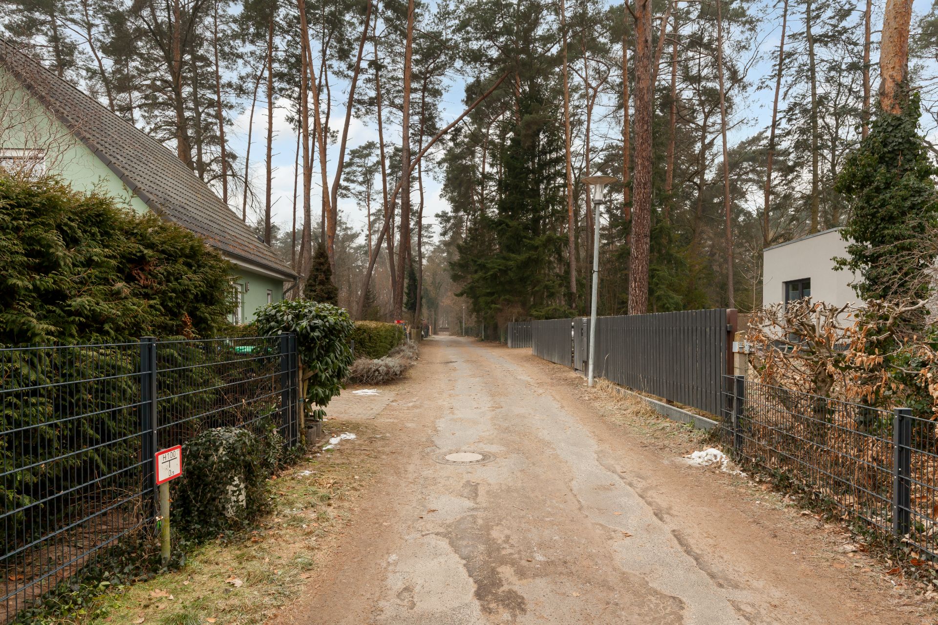 Unbefestigte Straße zwischen zwei Grundstücken mit Zäunen und Bäumen.