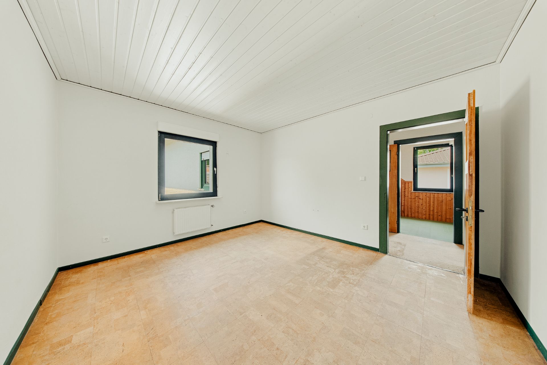 Leerer Raum mit weißem Wänden, Holzfußboden, Fenster und geöffneter Tür.