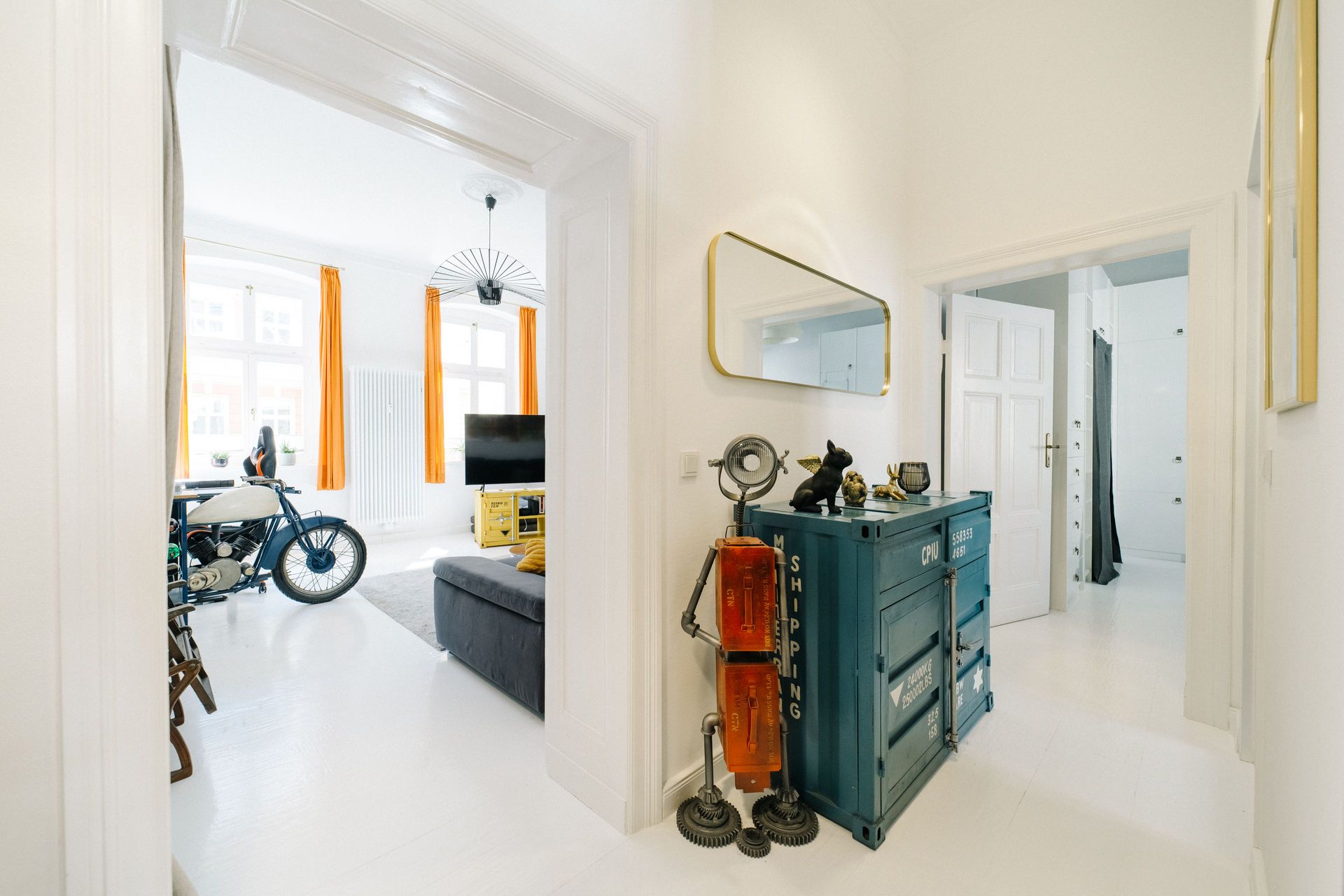 Heller Flur mit Spiegel, Deko, Blick ins Wohnzimmer mit Motorrad und Sofa.