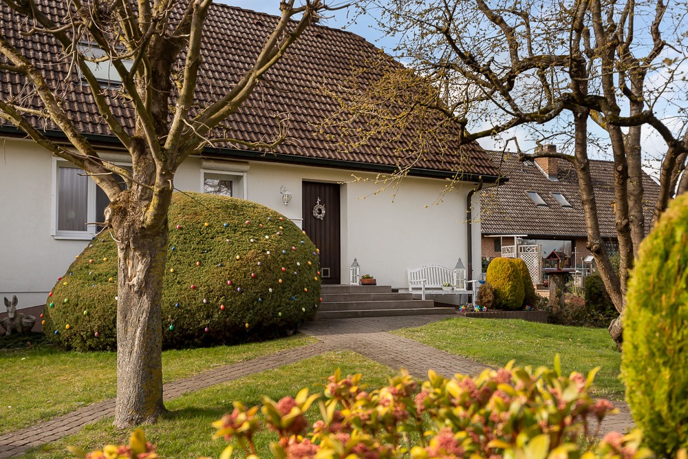 Haus mit braunem Dach, gepflegtem Garten, Sträuchern und Bäumen im Vordergrund.