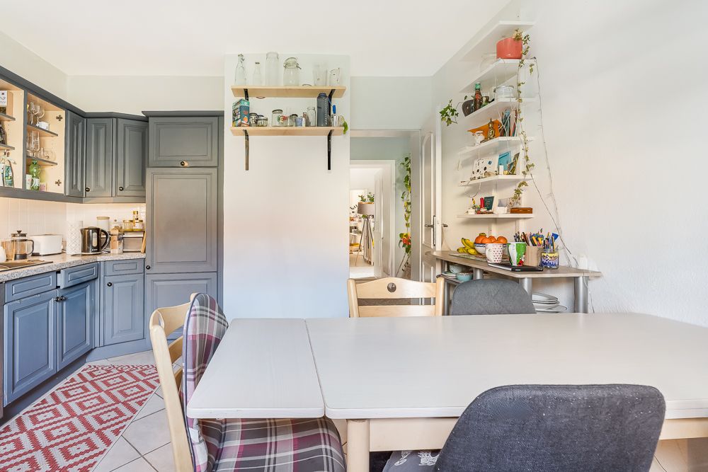 Essbereich mit Tisch und Stühlen, angrenzender Küche und Regal mit Pflanzen an der Wand.