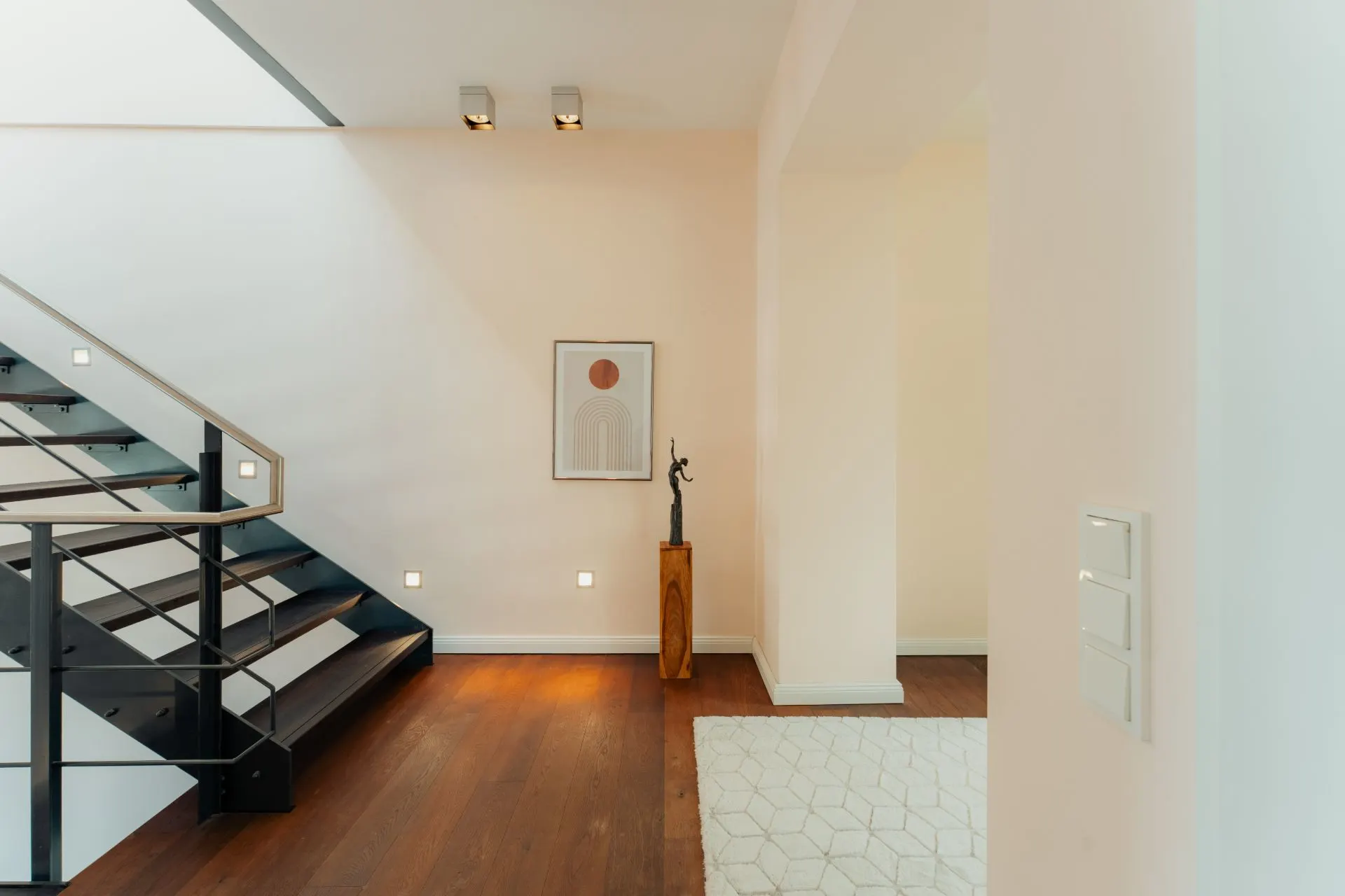 Heller Flur mit Holzfußboden, moderner Treppe und Wandbild.