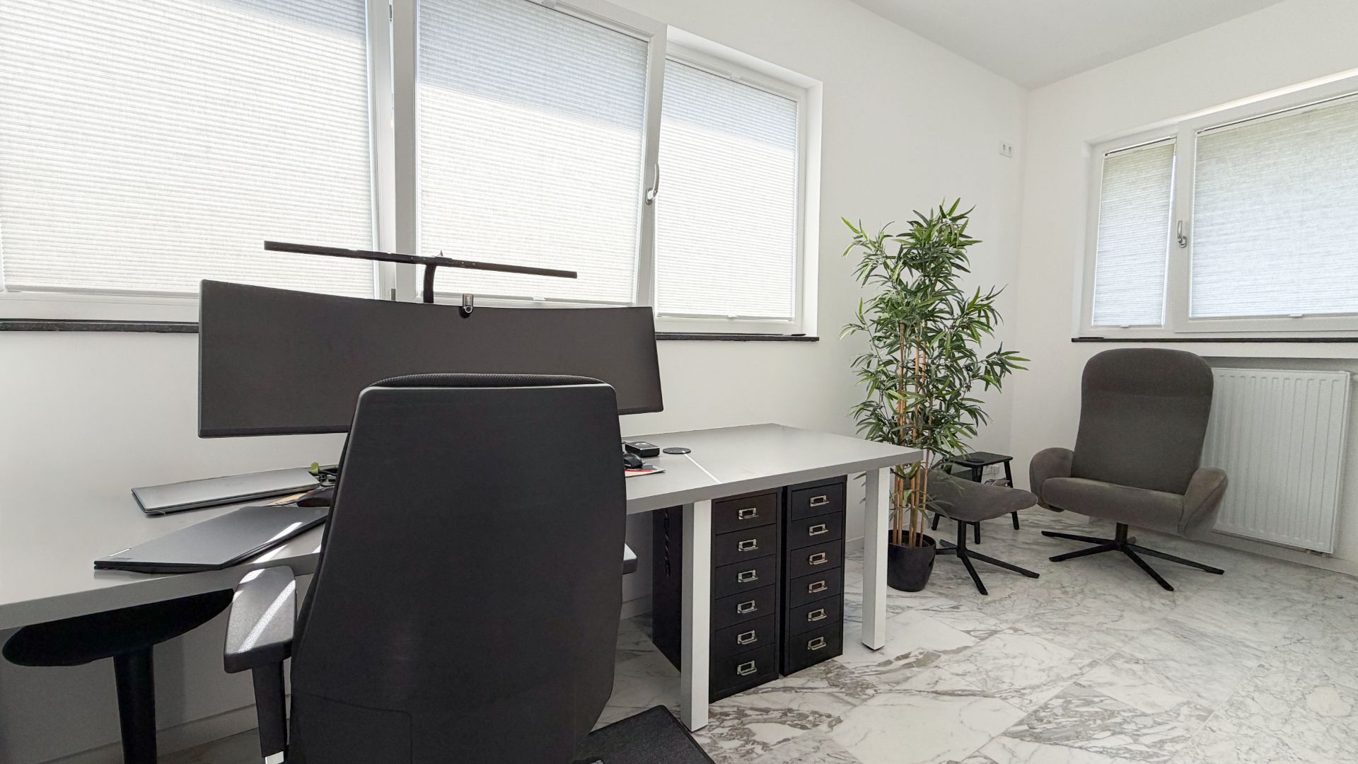 Helles Arbeitszimmer mit Schreibtisch, Bürostuhl, Sessel und Pflanze auf Marmorfußboden.