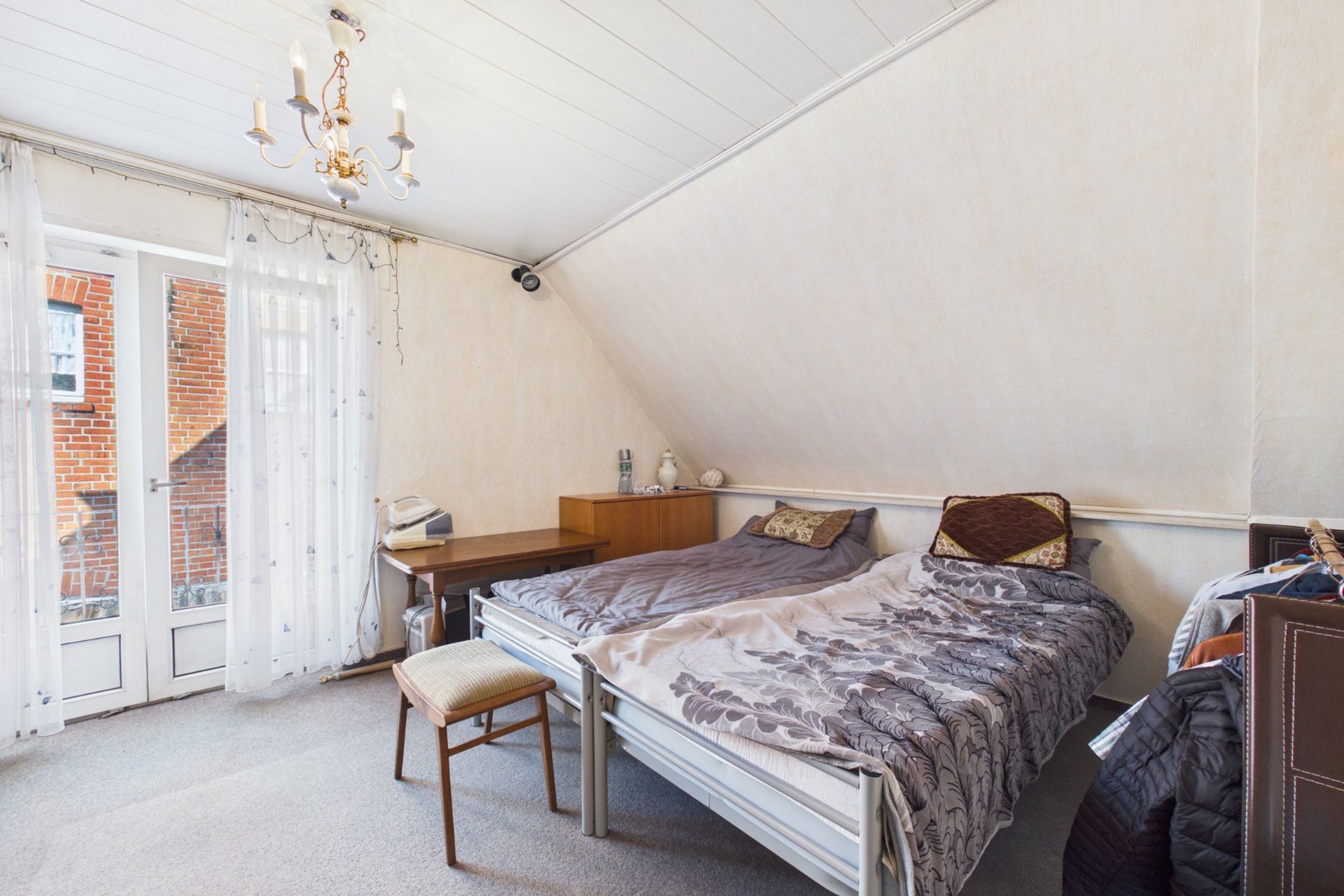 Helles Schlafzimmer mit Doppelbett, Schreibtisch, Stuhl und Zugang zu einem Balkon mit Glastüren.