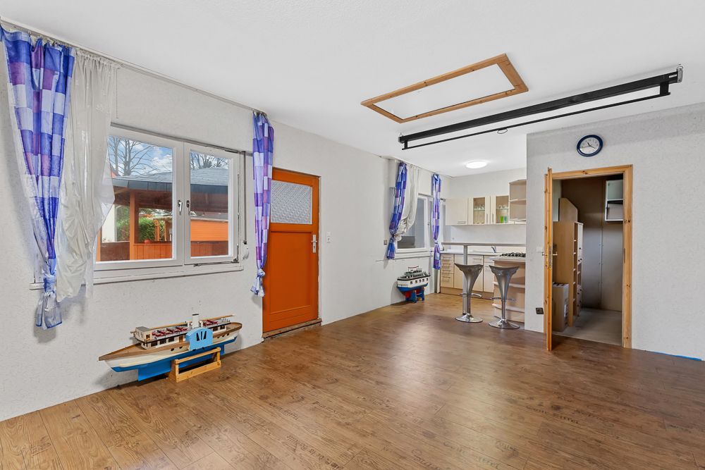 Wohnzimmer mit Holzfußboden, Modellen von Schiffen, offener Küche und blauen Vorhängen.