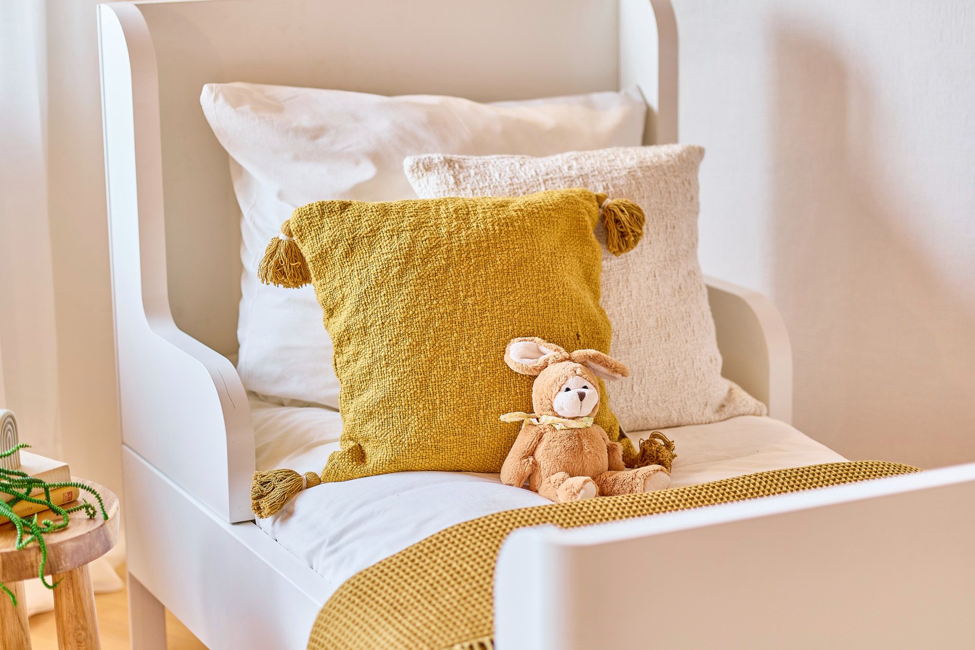 Weißes Bett mit gelbem Kissen, weißem Kissen und Kuscheltier auf einer gelben Decke.
