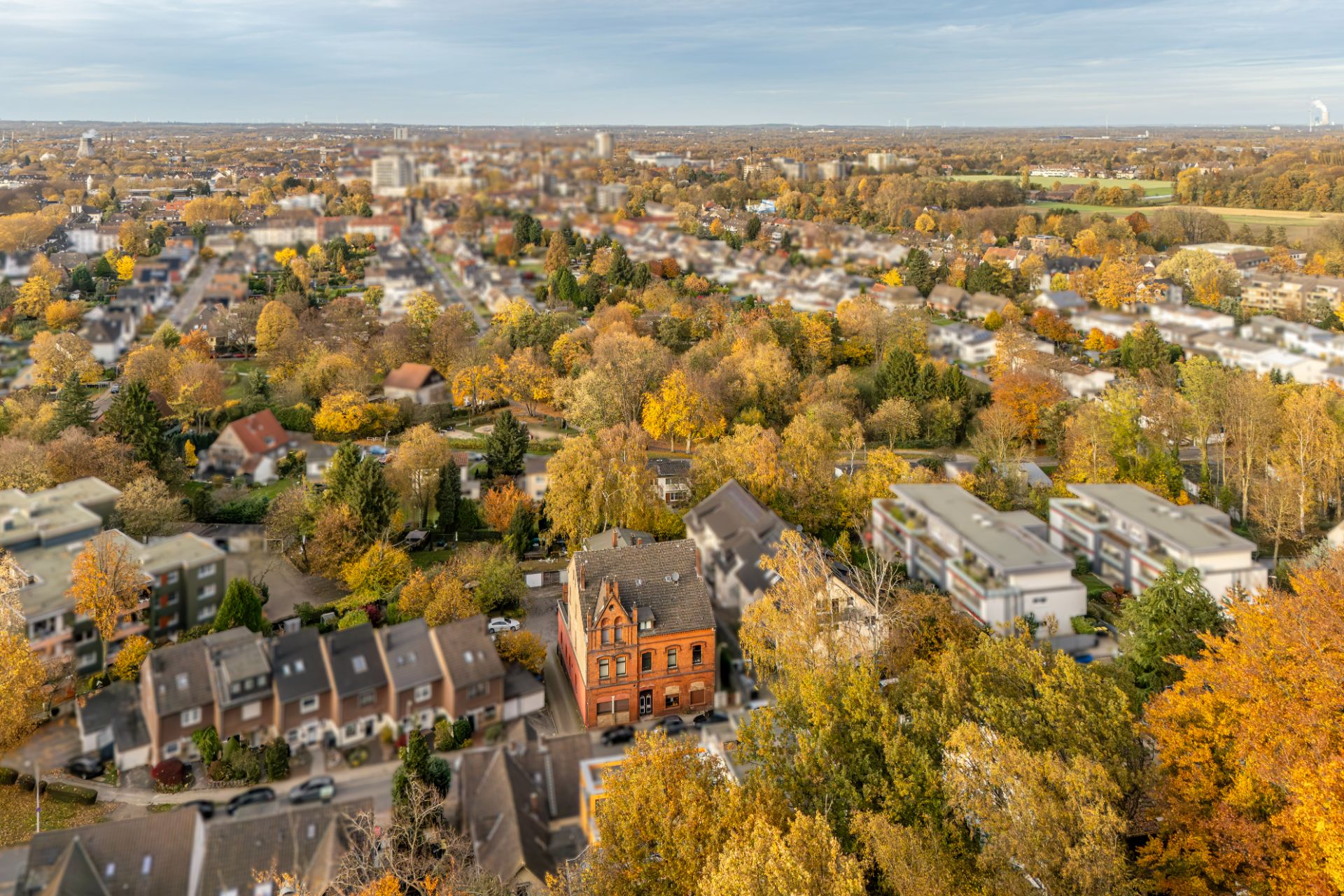 Luftaufnahme eines Wohngebiets mit vielen Bäumen und verschiedenen Häusern im Herbst.