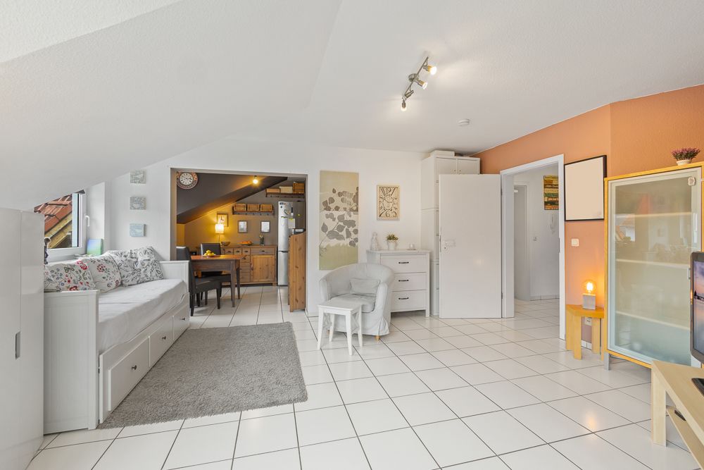 Helles Wohnzimmer mit Sofa, Teppich, Sessel und offener Blick in die Küche.