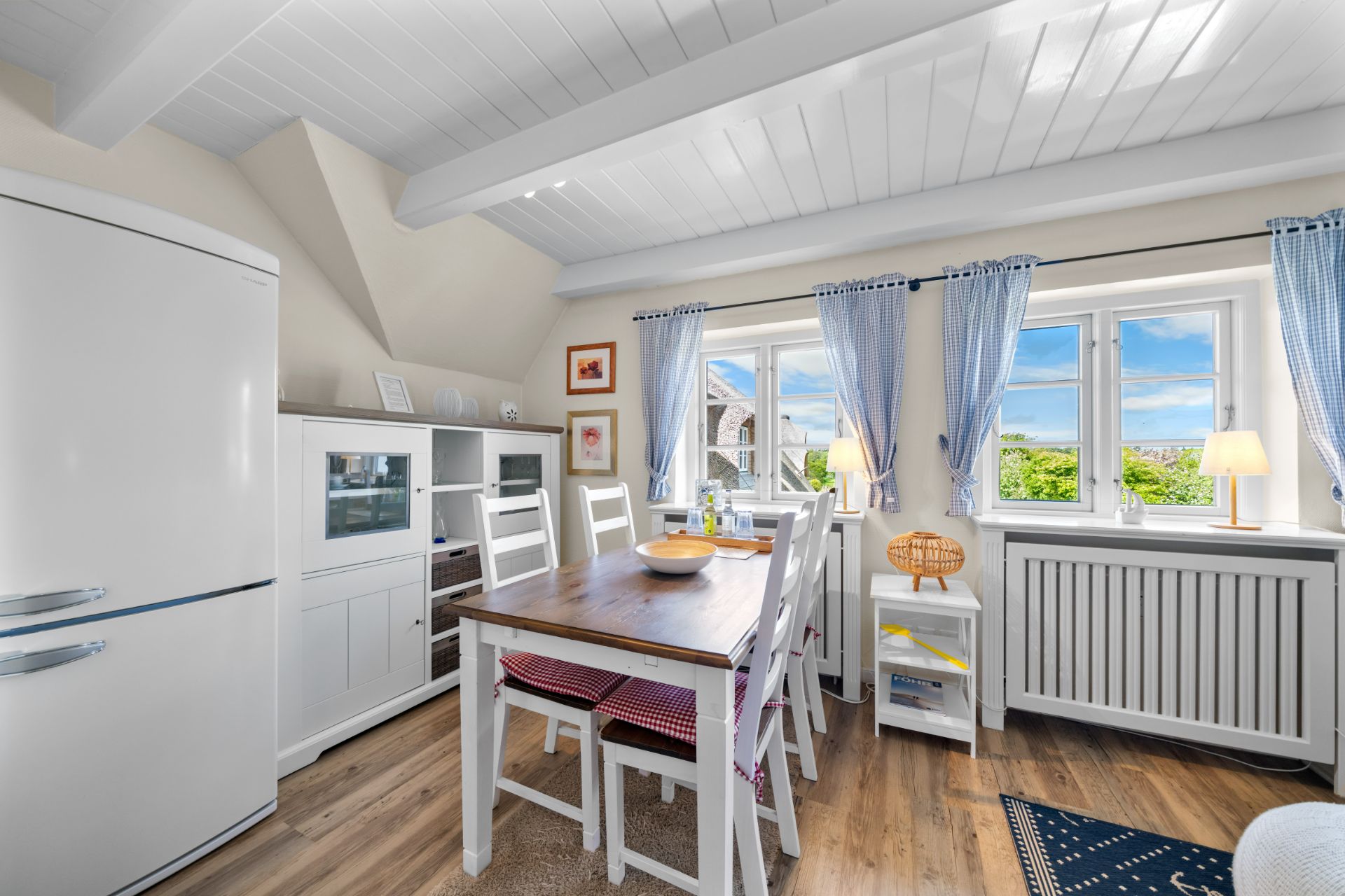 Heller Essbereich mit Holztisch, weißen Stühlen und großem Fenster mit blauen Vorhängen.