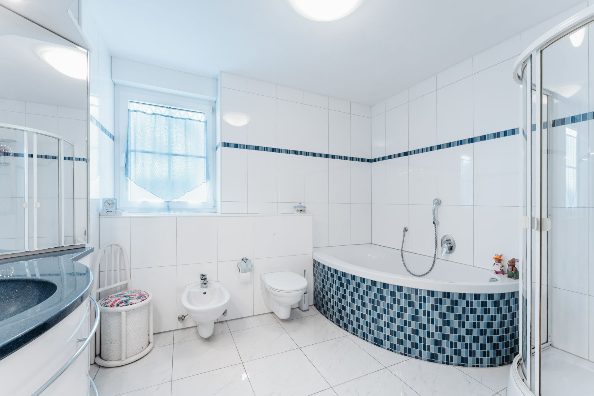 Modernes Badezimmer mit Eckbadewanne, Dusche, Bidet und WC, gefliest in Weiß und Blau.