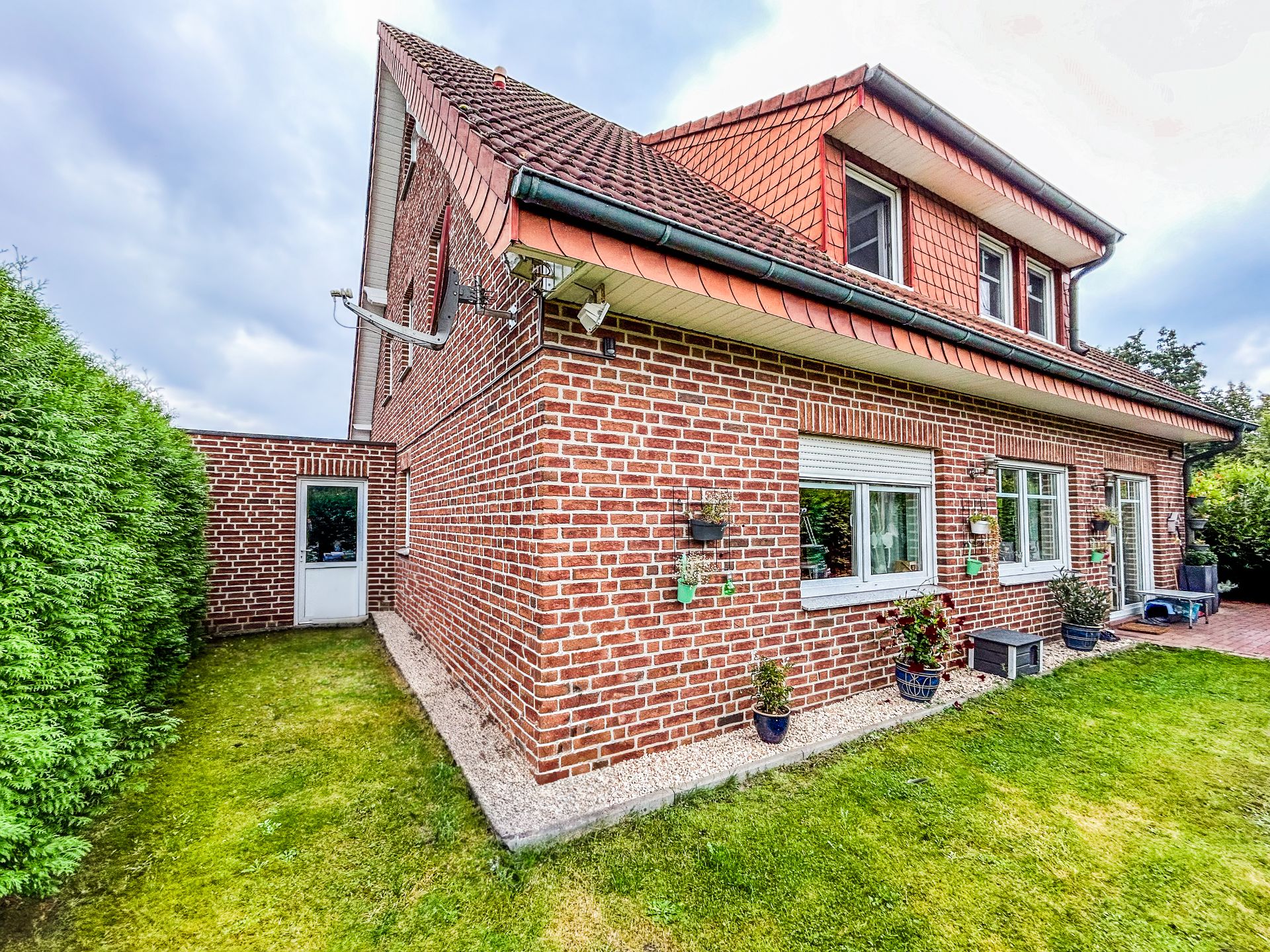 Backstein-Einfamilienhaus mit roten Dachziegeln, Garten und mehreren Fenstern.