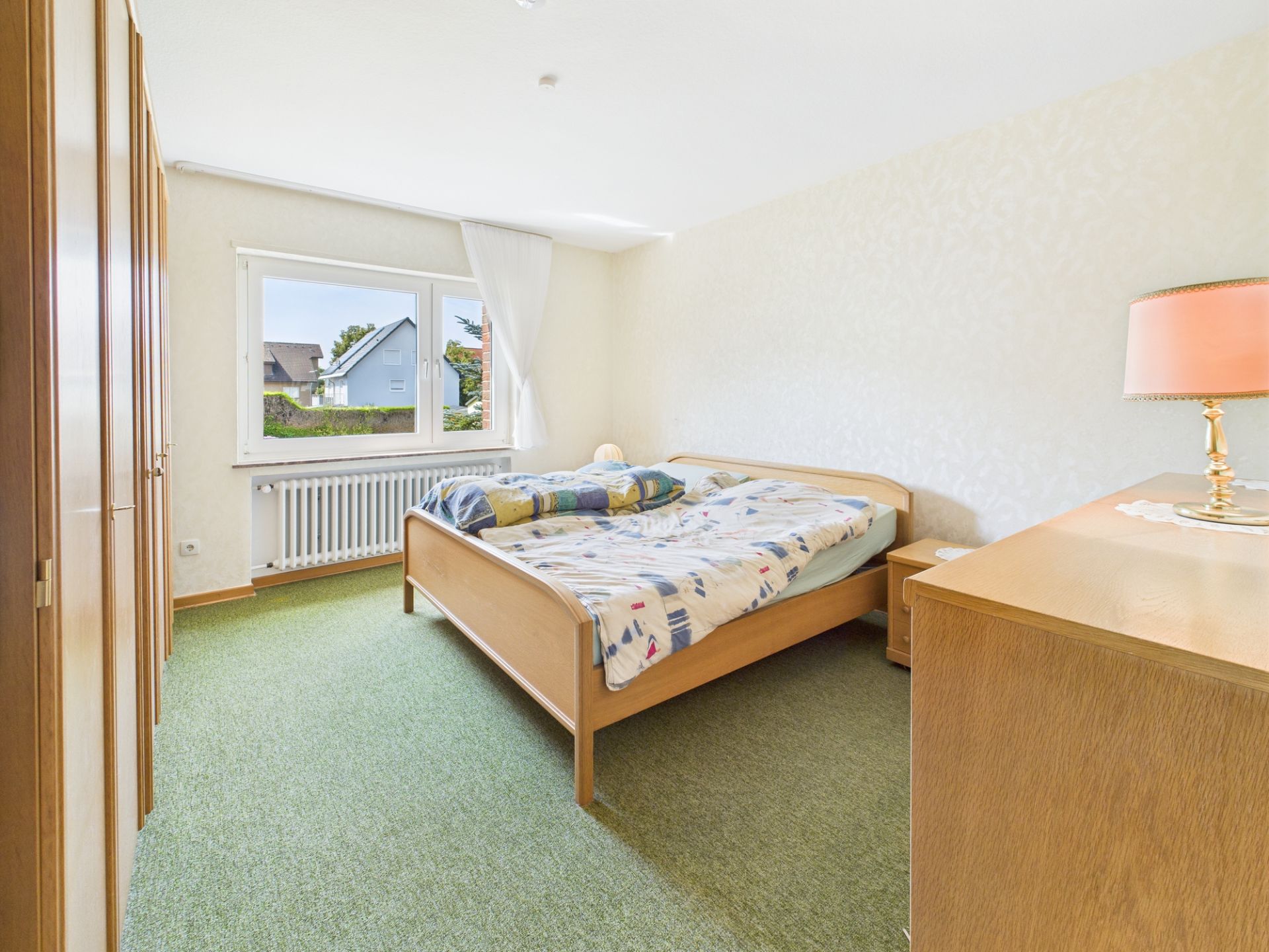 Helles Schlafzimmer mit Doppelbett, grünem Teppich und Holzmöbeln.