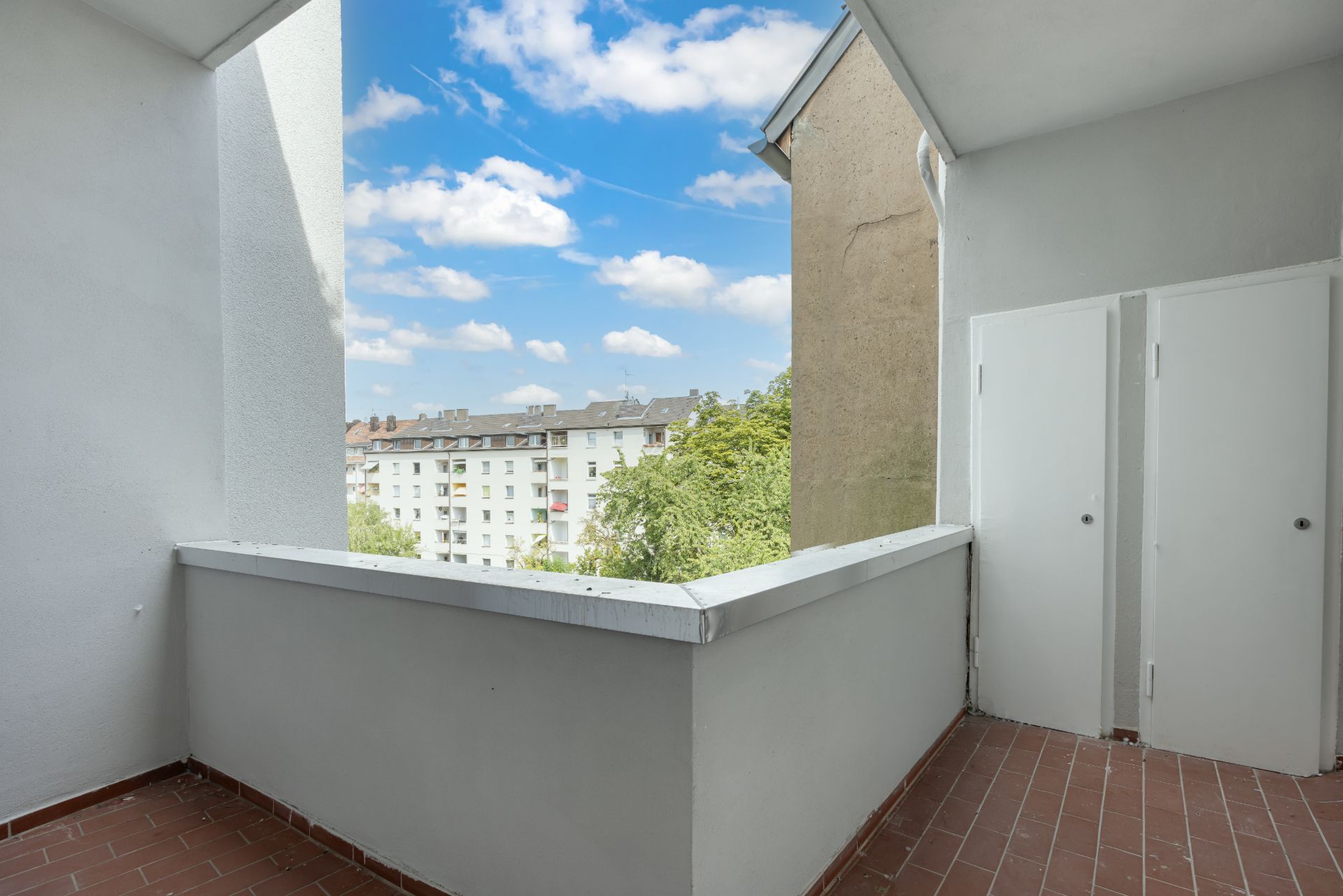 Überdachter Balkon mit Fliesenboden und Blick auf Wohnhäuser und Bäume.