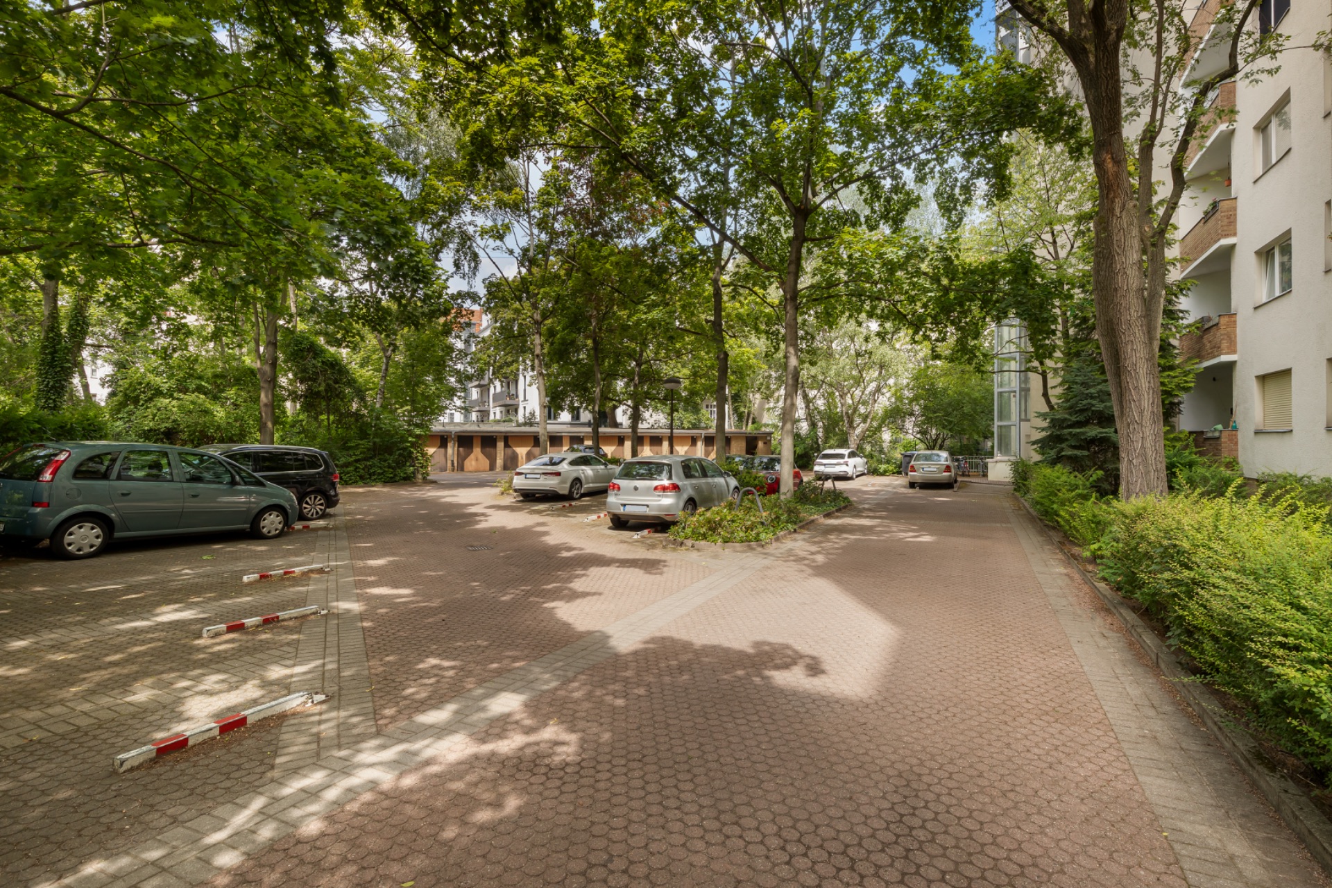 Parkplatz mit Autos und Bäumen vor Wohngebäuden an einem sonnigen Tag.